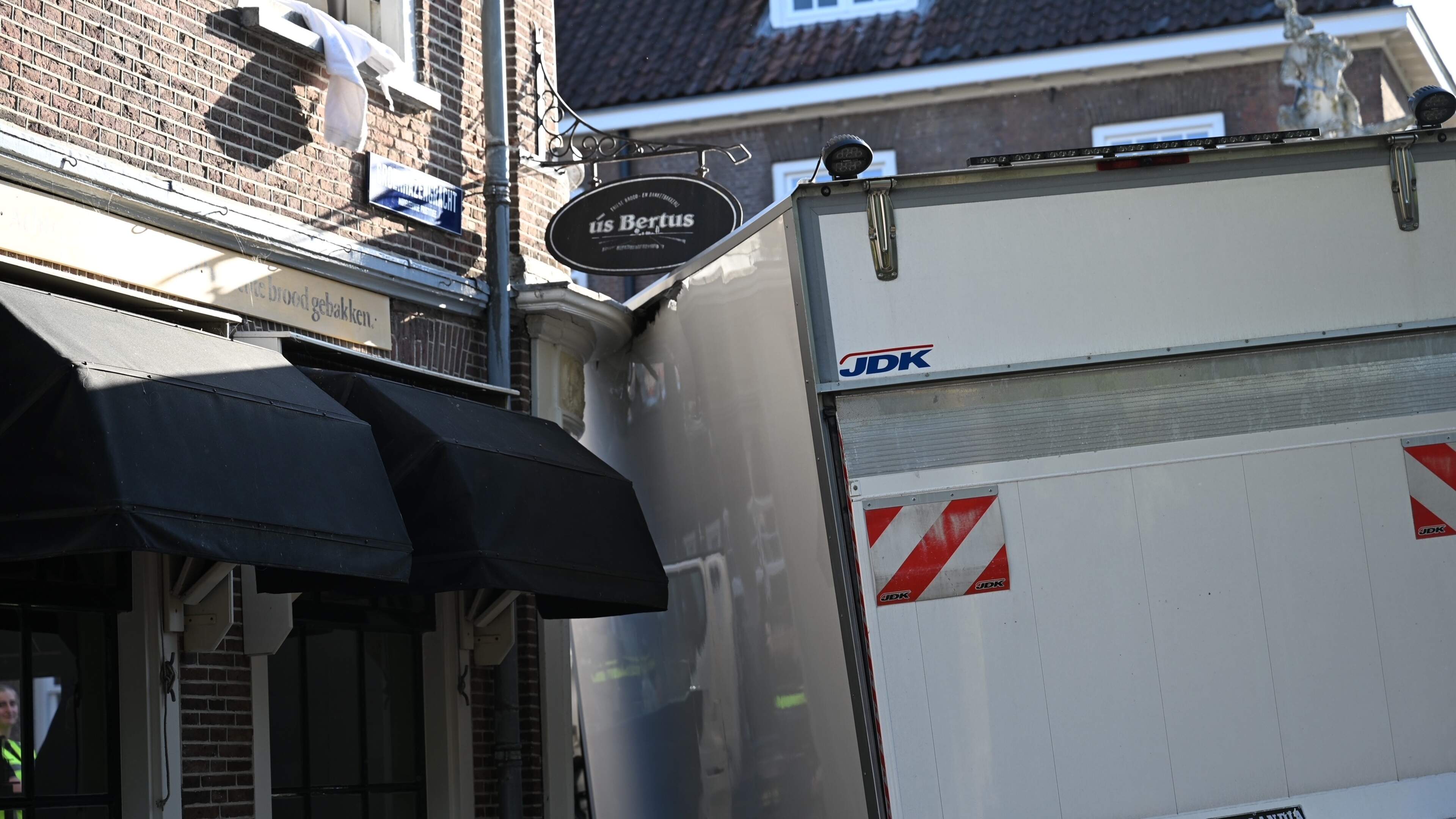 Bakwagen klemgereden tegen gevel van bakkerij op gracht in centrum van Leiden